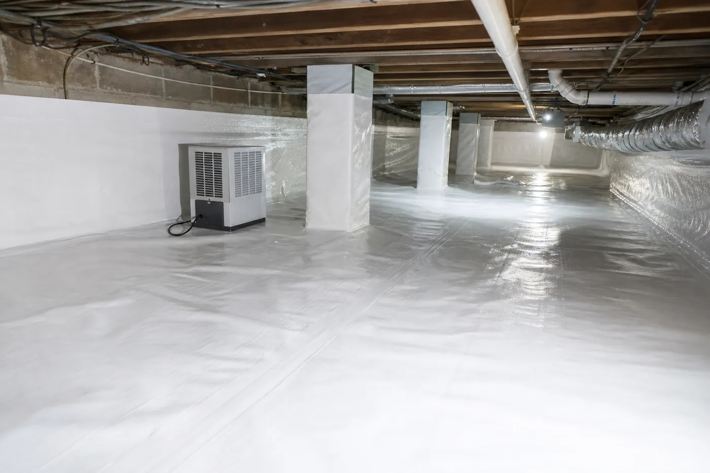 Crawl space dehumidifier on a white vapor barrier in a sealed crawl space with wrapped support piers